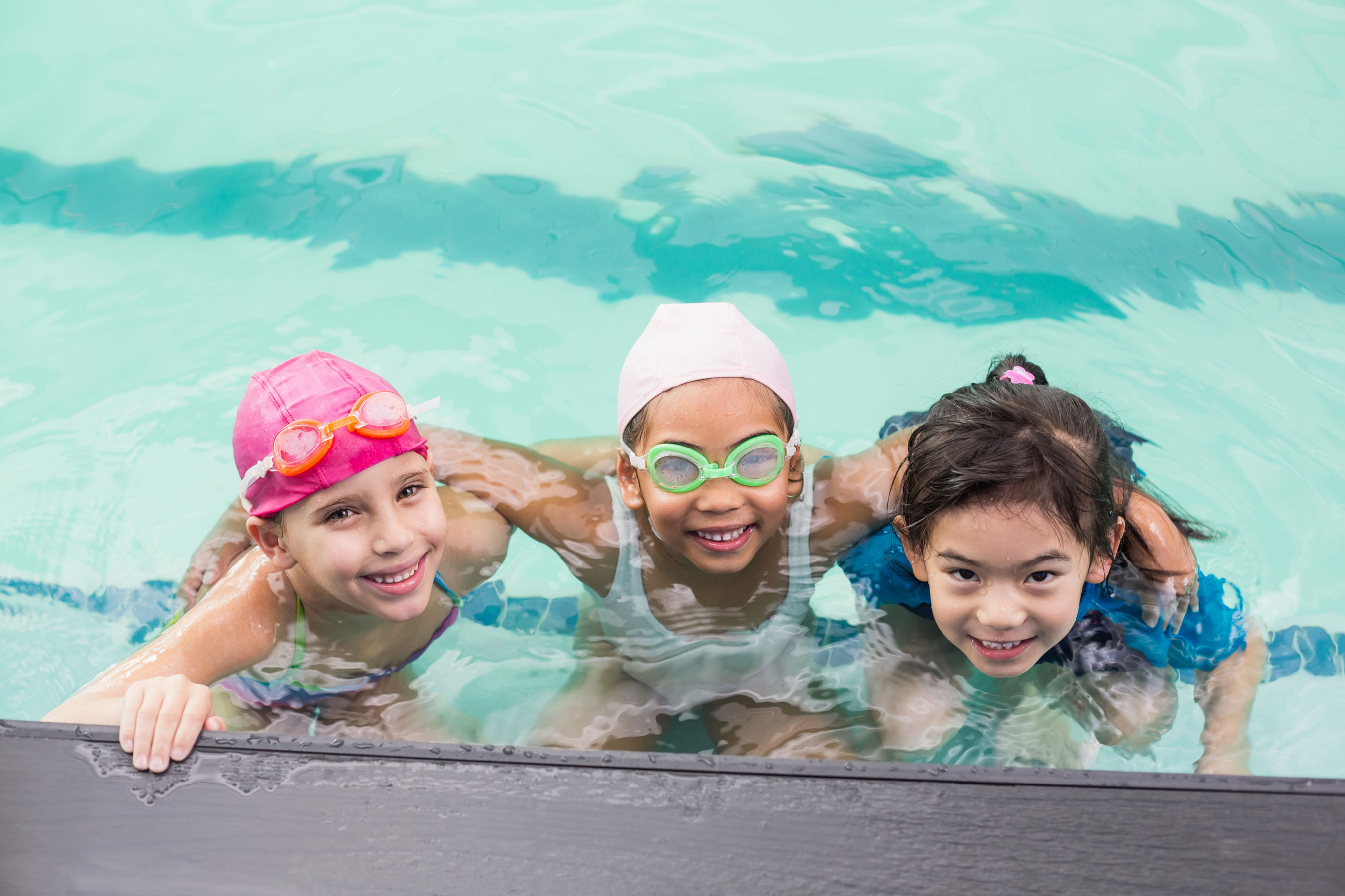 three children in the pool water smiling at the camera